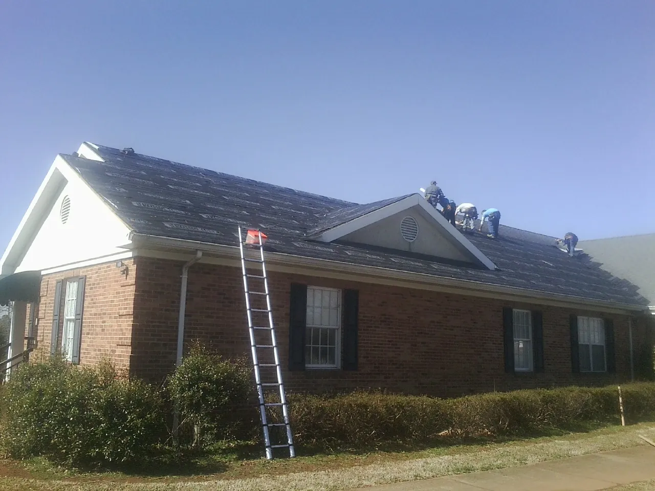 Crew tearing shingles off a brick ranch roof with a ladder set — Emergency Roof Repair work by our crew in Evergreen